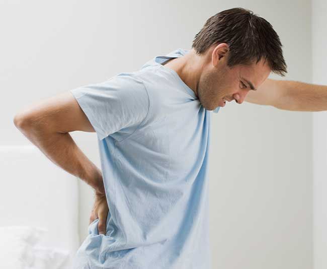 Chiropraktik Ulm Schmerzbehandlungen Mann mit Rückenschmerzen lehnend an der Wand